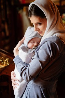 beautiful mom in a headscarf with a small child in her arms in church. 