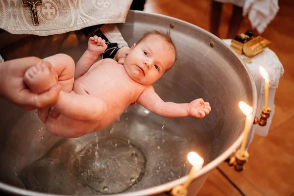 Ein Kind wird bei einer christlichen Taufe in der Kirche in einem Brunnen ins Wasser gelassen — Stockfoto