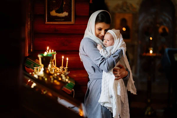 Hermosa mamá en un pañuelo para la cabeza con un niño pequeño en sus brazos en la iglesia. —  Fotos de Stock