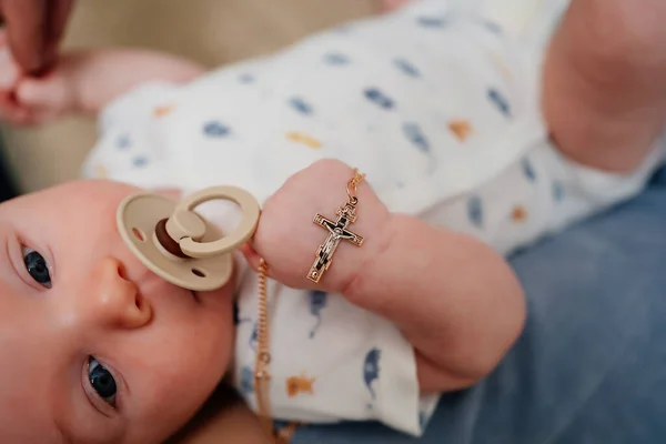 Baby mit einem goldenen Kreuz an einer Kette in der Hand. Christlicher Glaube. — Stockfoto