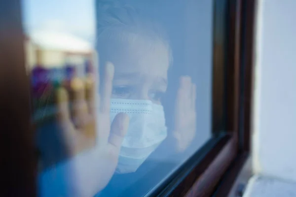 A través del vidrio. niña en máscara protectora, mirar por la ventana exterior. — Foto de Stock