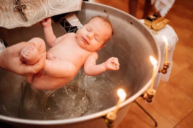a child is lowered into the water in a font at a Christian baptism in the church
