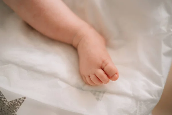 Pierna de bebé en una sábana blanca. cuidado de la piel y corte de uñas en recién nacidos. —  Fotos de Stock