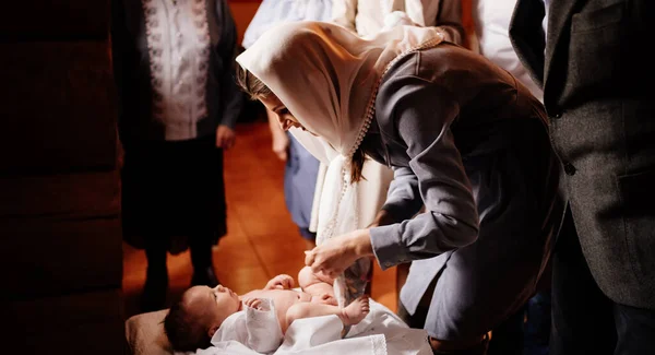 Мама одевает своего ребенка на стол в церкви. таинство крещения. — стоковое фото