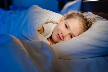 a cute girl is lying in bed and smiling. calm and healthy childrens sleep