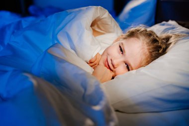 a cute girl is lying in bed and smiling. calm and healthy childrens sleep