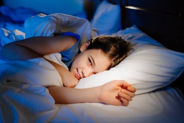 Bir kız yatakta yatıyor ve gülümsüyor. Sakin ve sağlıklı çocuklar uyur.