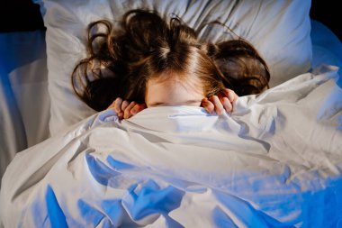 Korkmuş kız, odasında battaniyeyle yüzünü örtüyor. Çocuklar korkar.