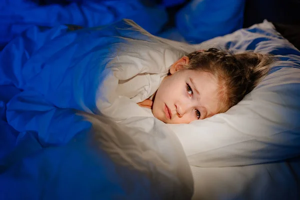 Uma menina está deitada na cama e com medo de adormecer depois de assistir a um filme de terror. — Fotografia de Stock