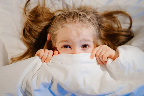 Ir arriba Vista. Niña se acuesta en la cama, asustada y cubre la cara con manta — Foto de Stock