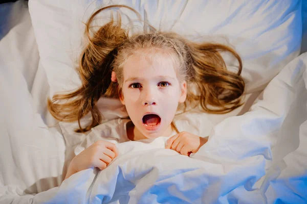 Ir arriba Vista. La niña se acuesta en la cama y asustada. miedo de los niños. — Foto de Stock