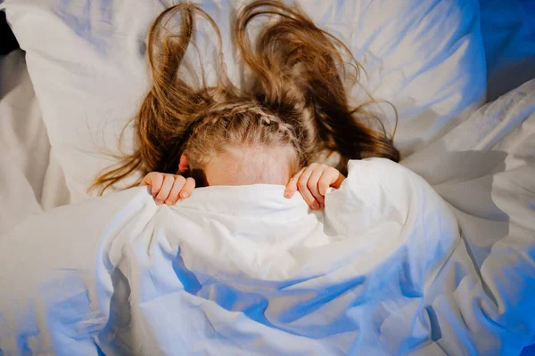Vista dall'alto. La bambina giace a letto, spaventata e copre il viso con una coperta — Foto Stock