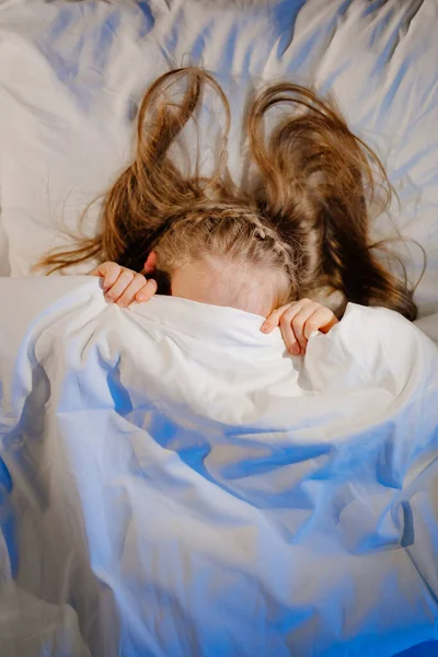 Vista dall'alto. La bambina giace a letto, spaventata e copre il viso con una coperta — Foto Stock