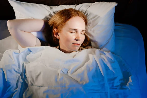 Vista dall'alto. una donna con i capelli rossi dorme a letto e vede sogni tranquilli, sorrisi. — Foto Stock