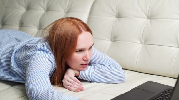 Nő dolgozik, miközben otthon fekszik a kanapén egy laptopon — Stock videók