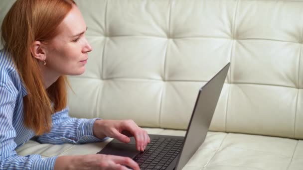 Femme travaille alors qu'elle est allongée sur le canapé à la maison sur un ordinateur portable — Video