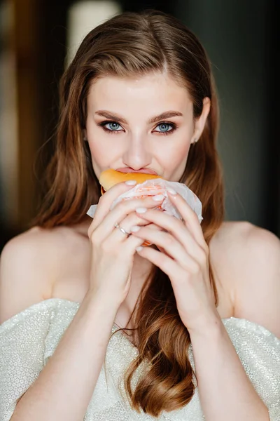 긴 머리에 화장을 하고 햄버거를 먹고 있는 아름다운 젊은 여자. — 스톡 사진