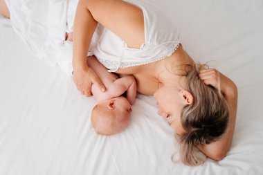 Anne, anne sütü içtikten sonra bembeyaz bir yatakta bir bebekle yatıyor.. 