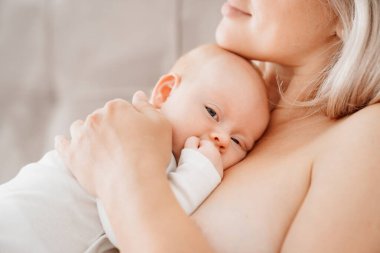 Anne, anne sütü içtikten sonra bembeyaz bir yatakta bir bebekle yatıyor.. 