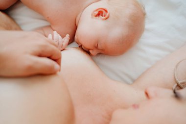 Kapat. Kadın beyaz bir yatakta bebekle anne sütüyle besleniyor.. 