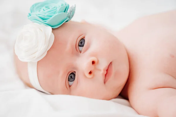 Schattig roodharig baby dragen van een hoofdband ligt op een wit bed. — Stockfoto