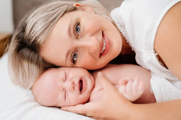 Mãe é mãe está deitada com um bebê em uma cama branca depois de alimentar o leite materno. — Fotografia de Stock