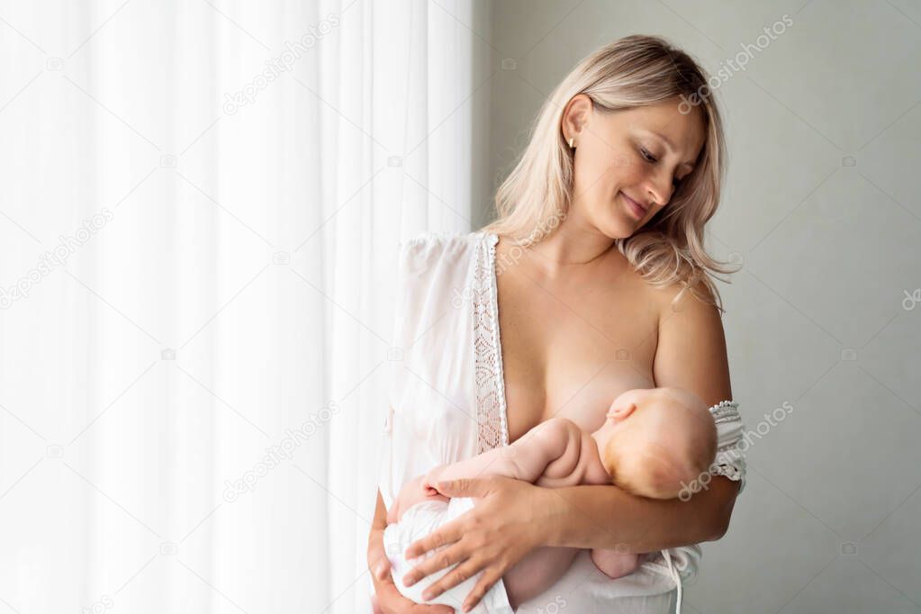 mom feeds baby standing at the window. breast-feeding.
