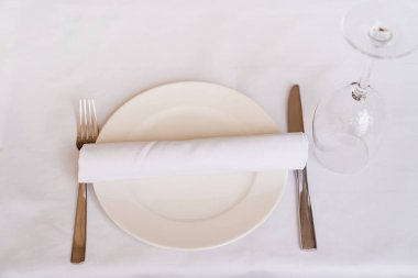 table setting. empty white plate, towel, Cutlery, and upturned wine glass.