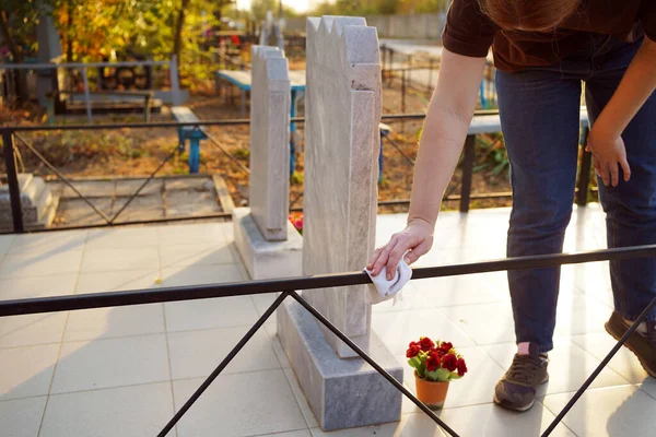 Mezarlığı temizliyorum. Bir kadın mezardaki siyah çitleri paçavrayla yıkıyor..