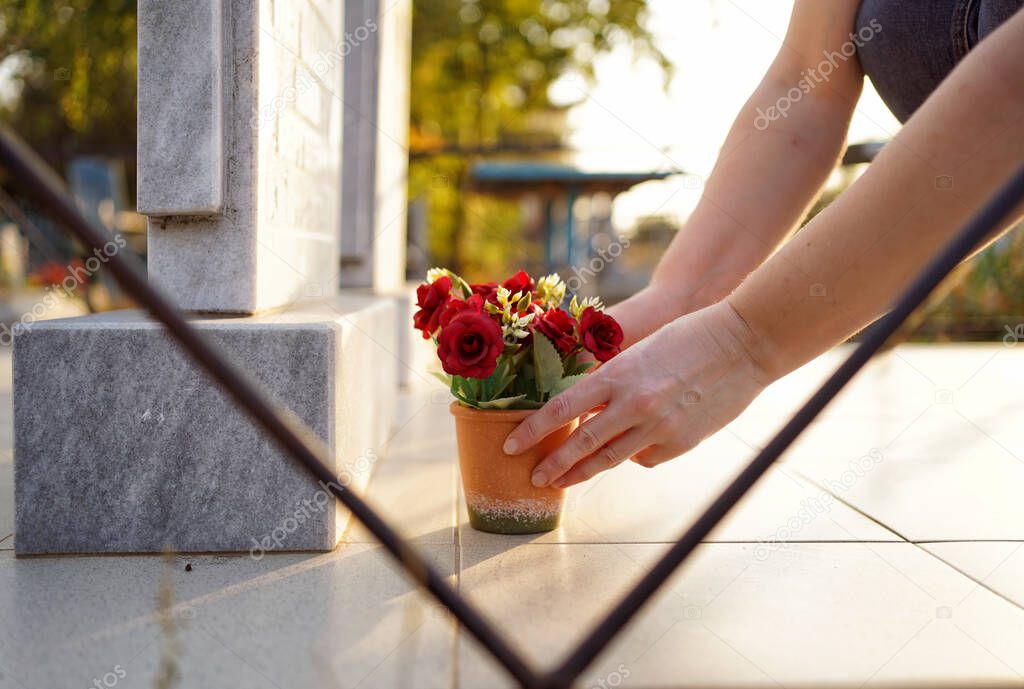 hands put a pot of artificial flowers near the monument in the cemetery. 