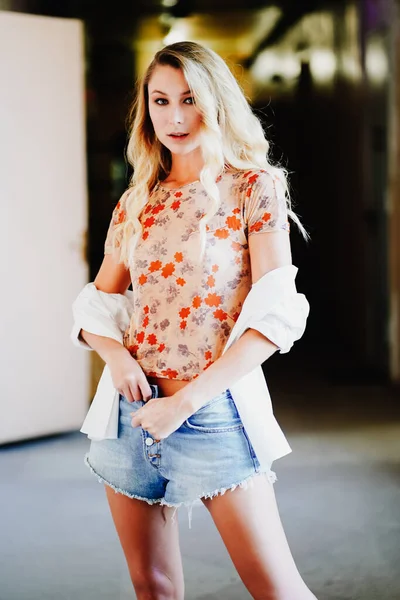 Hermosa joven con el pelo largo y rubio en una camisa blanca y pantalones cortos de mezclilla. —  Fotos de Stock