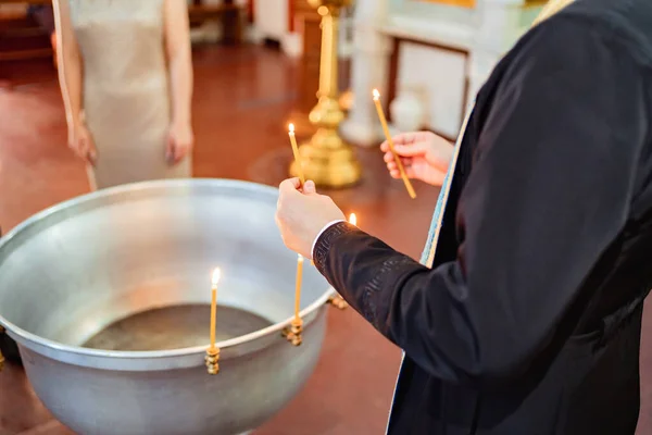Священник держит свечи в руках возле купели для крещения. — стоковое фото