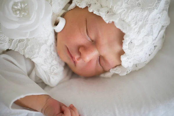 Un bebé recién nacido con ropa blanca y un sombrero está durmiendo. — Foto de Stock