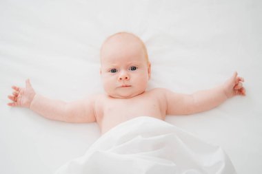 Sevimli kızıl saçlı bebek beyaz bir yatakta yatıyor. Bebek bakımı kavramı