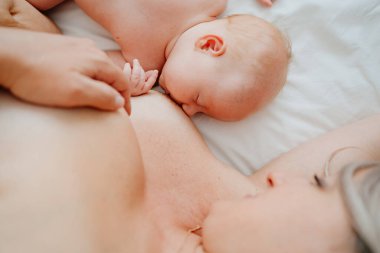 Kapat. Kadın beyaz bir yatakta bebekle anne sütüyle besleniyor.. 