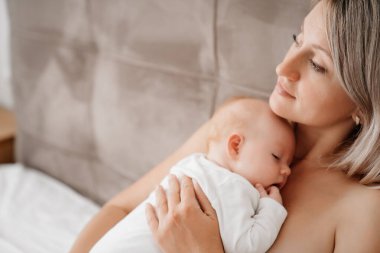 Anne, anne sütü içtikten sonra bembeyaz bir yatakta bir bebekle yatıyor.. 