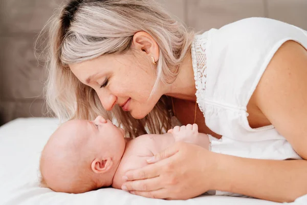 Mama este mama este culcat cu un copil într-un pat alb după hrănirea laptelui matern . — Fotografie, imagine de stoc