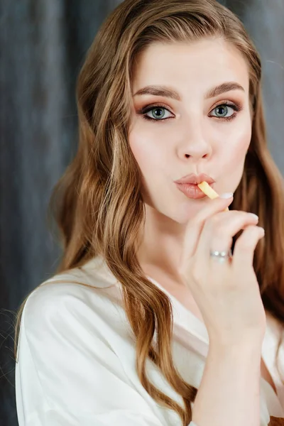 Vacker ung kvinna med långt hår och makeup äta pommes frites. — Stockfoto