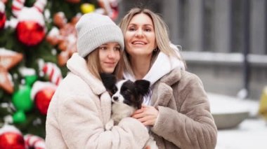 Güzel anne-kız ve köpek Papillon sokakta Noel ağacının yanında.