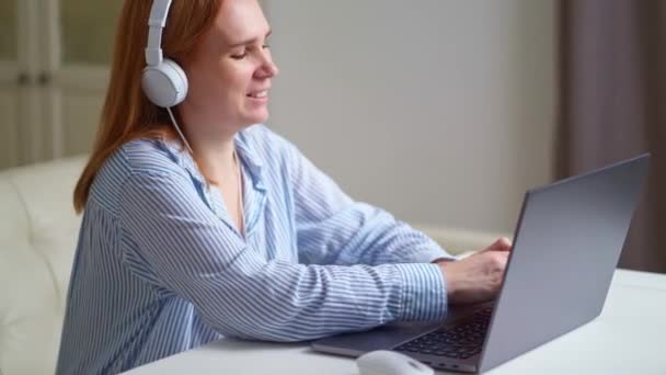 Nő fülhallgatóval dolgozik otthon egy laptop, hallgat és körvonalaz egy előadást — Stock videók