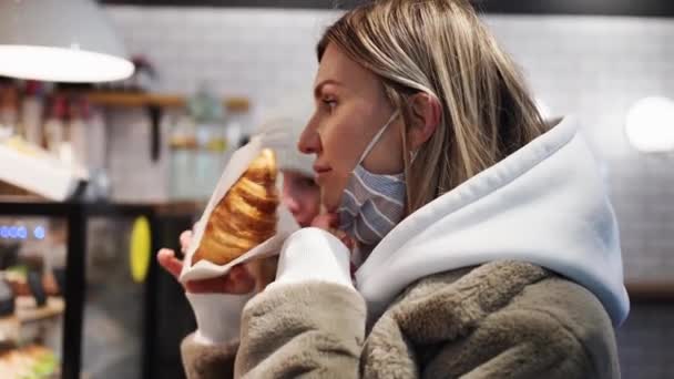 Frau mit Schutzmaske sorgt im Café für Ordnung, schnuppert ein Croissant — Stockvideo