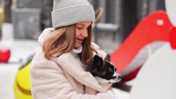 Όμορφο κορίτσι με σκύλο Papillon στην αγκαλιά της στους χειμερινούς δρόμους των Χριστουγέννων — Αρχείο Βίντεο
