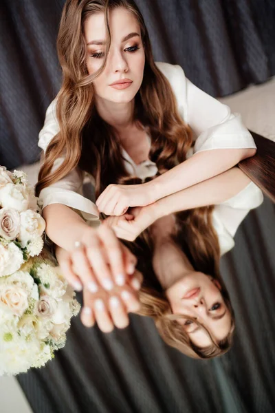 Hermosa mujer en túnica blanca, con ramo de mentiras y se refleja en el espejo. — Foto de Stock