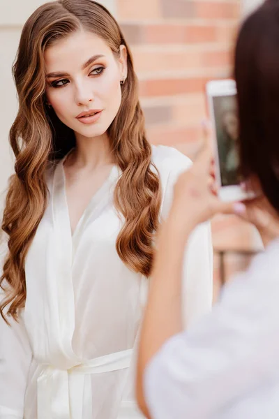 A beautiful woman in white clothes is photographed on phone for social networks. — Stock Photo, Image