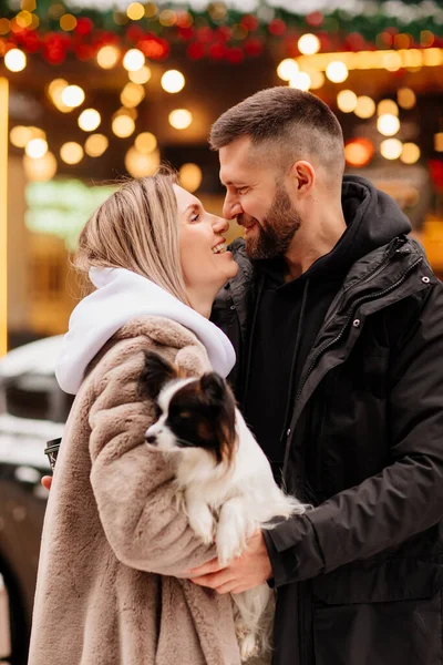 Belo casal com cão Papillon perto de vitrines de Natal. sessão de fotos — Fotografia de Stock