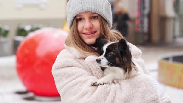 Menina bonita com cão Papillon em seus braços nas ruas de Natal de inverno — Vídeo de Stock