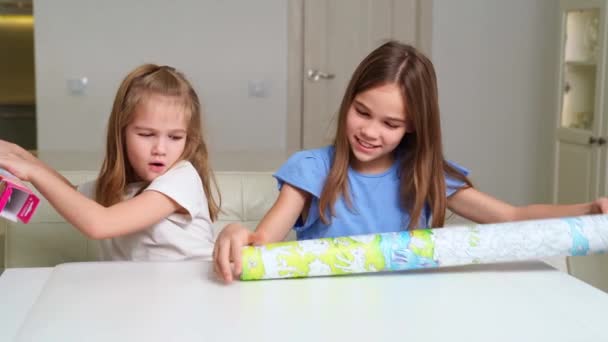 Two cute girls unpack and unwrap a large poster coloring with unicorns. — Stock Video