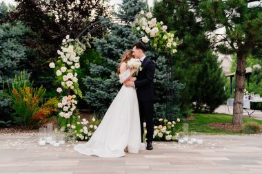 Yaşayan çiçeklerin kemerinde düğün töreni. Güzel yeni evliler şefkatle kucaklaşır.