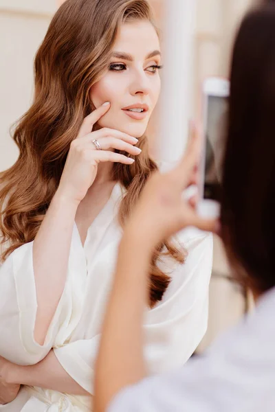 Uma mulher bonita em roupas brancas é fotografada no telefone para redes sociais. — Fotografia de Stock