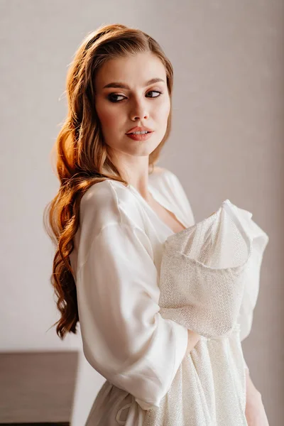 Retrato de mulher bonita em roupão branco segurando vestido de noiva na frente dela — Fotografia de Stock